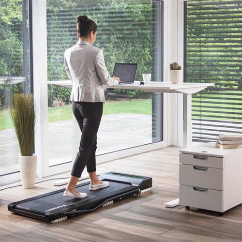 kvinde bruger Top Sport CS 2000 Walking Pad imens at hun står ved et skrivebord og arbejder.